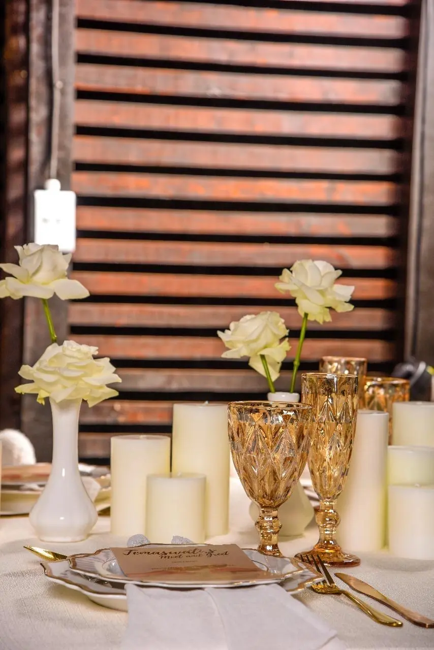 Table decor of wine glasses, white roses and cream pillar candles.