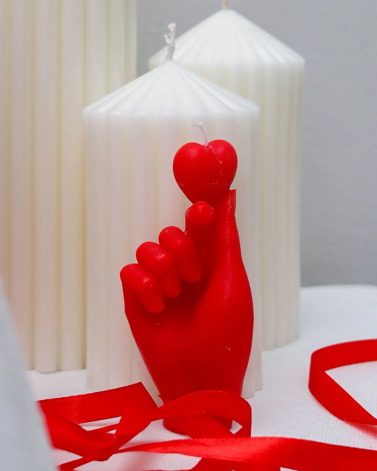 Red candle of a hand holding up a heart at the tip of fingers.