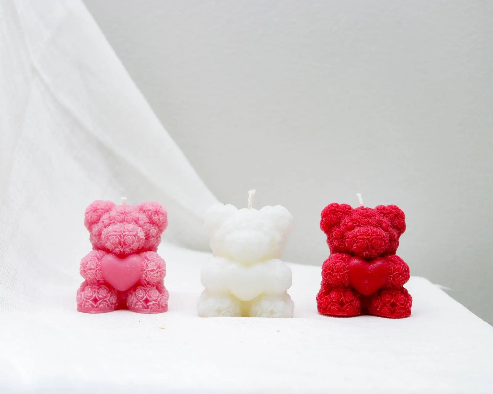 Candles of small pink, white and red teddy bears holding a heart in their hands.